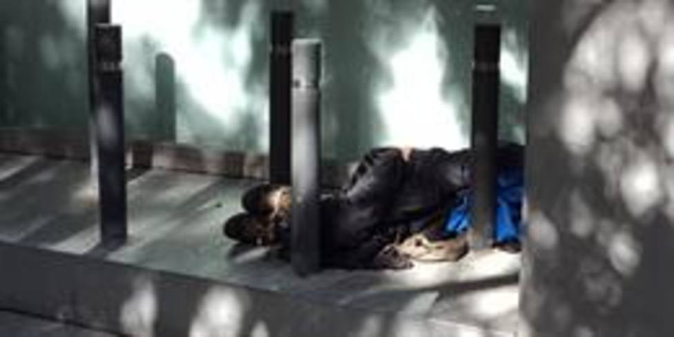 Un joven durmiendo en la calle entre bolardos