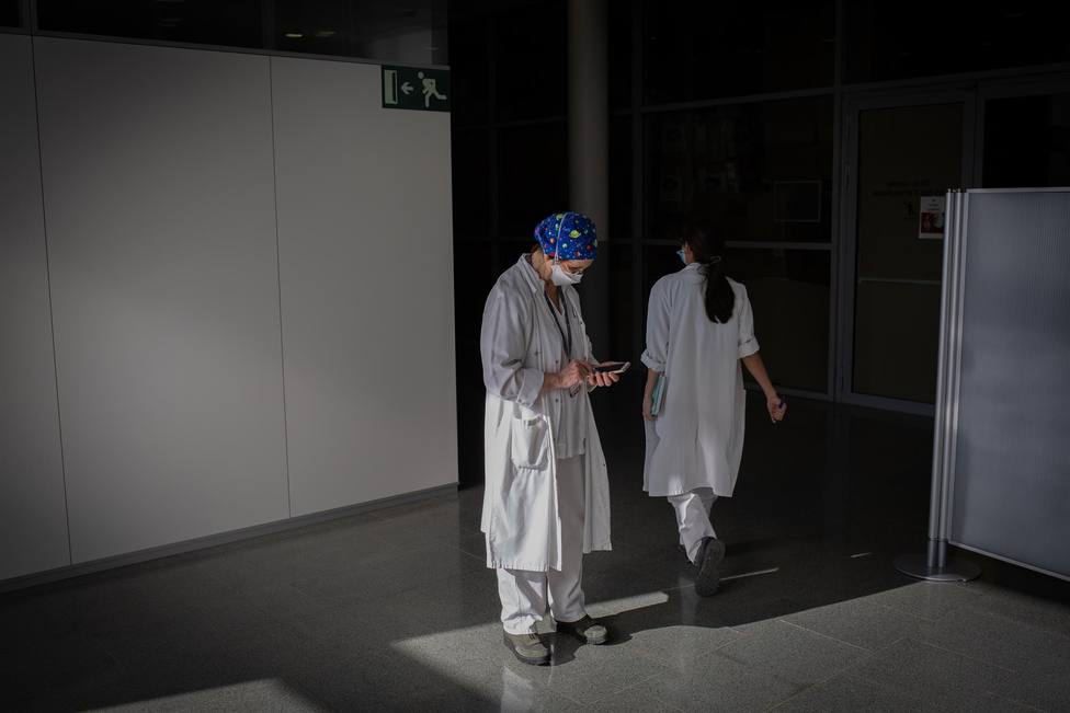 Una enfermera consulta su teléfono mientras la otra camina a través del pasillo