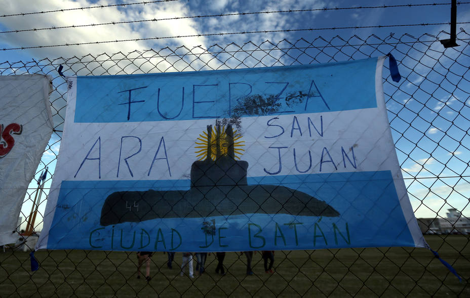 People walk behind an Argentine national flag displayed on a fence in Mar del Plata
