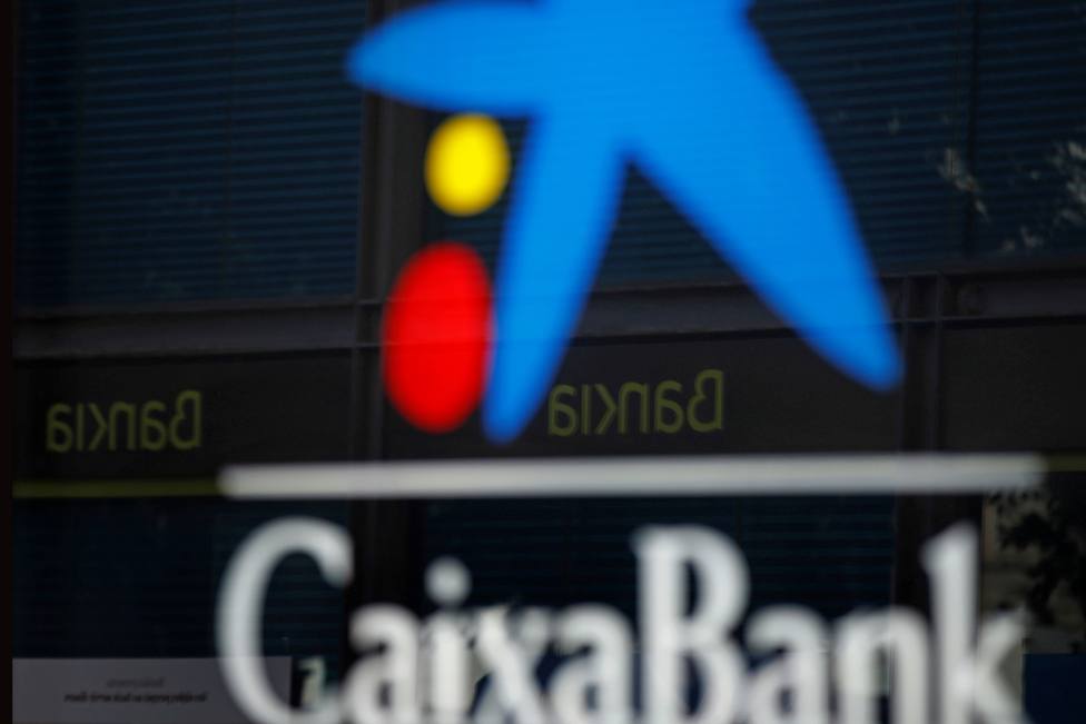 Vista de una oficina de CaixaBank y otra de Bankia reflejada en el cristal - FOTO: EFE / Toni Albir