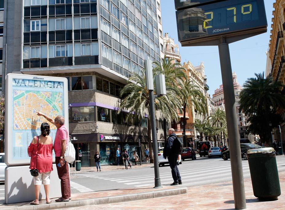 Dos jóvenes pasan ante un termómetro que marca 27 grados en el centro de Valencia