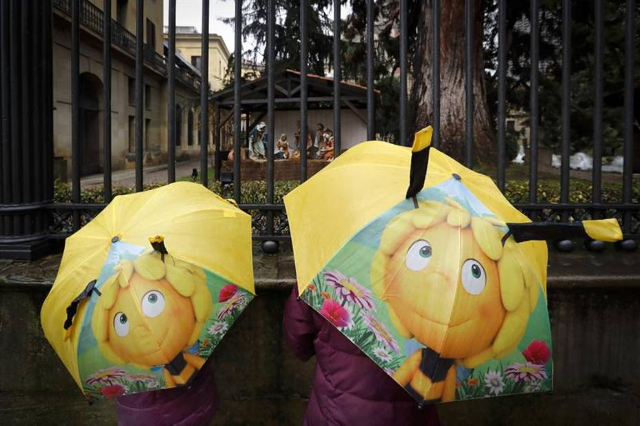 Dos niñas se protegen de la lluvia bajo sendos paraguas mientras observan uno de los belenes que Pamplona