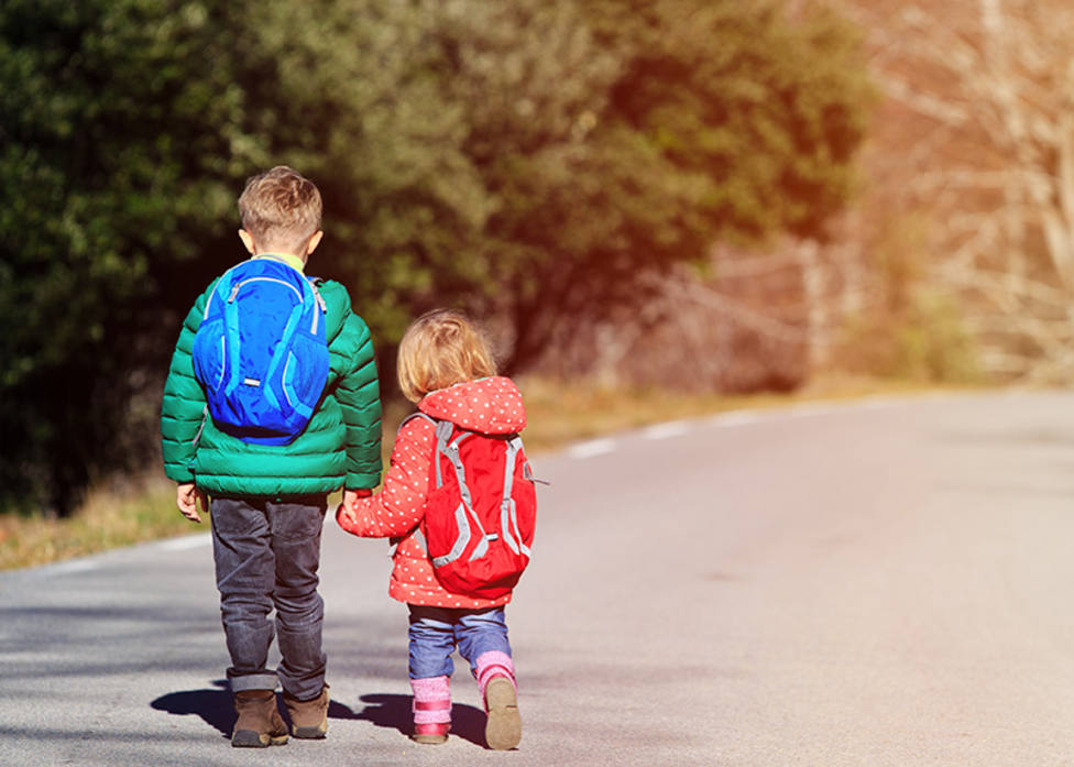 brother and sister with backpacks walking on the road