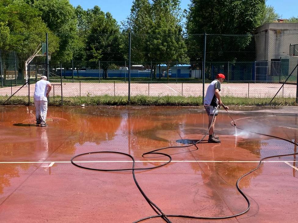 Dos operarios municipales limpian una de las pistas polideportivas de Xinzo