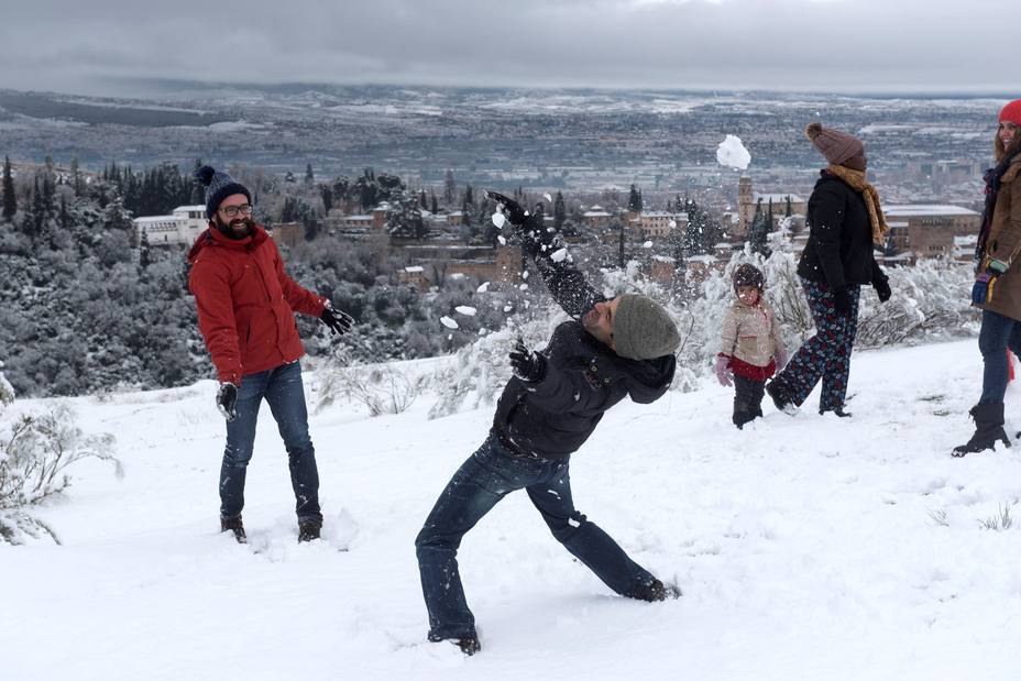 Varias personas juegan con la nieve con la Alhambra de Granada de fondo, que ha recibido una intensa nevada