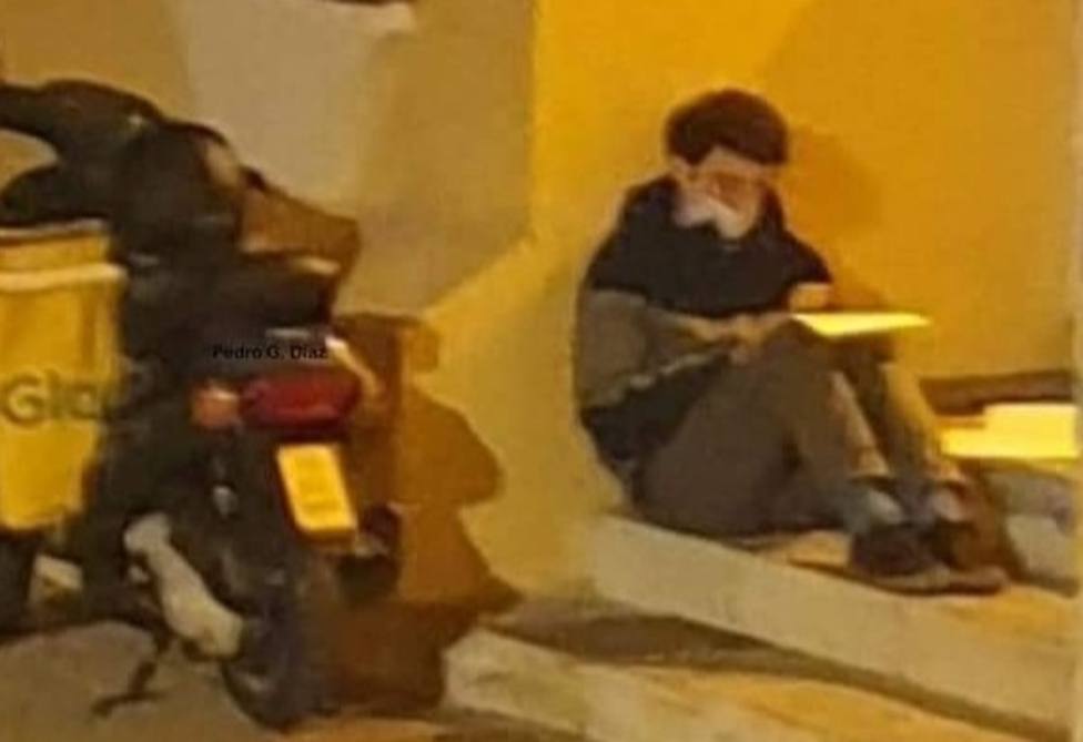 Un joven repartidor de Glovo estudia bajo la luz de una farola de Málaga mientras espera su próxima entrega