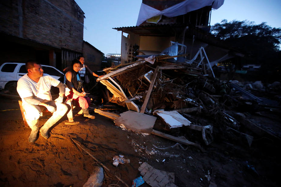 A family sitting outside their house destroyed after heavy rains caused several rivers to overflow, pushing sediment and rocks into buildings and roads in Mocoa