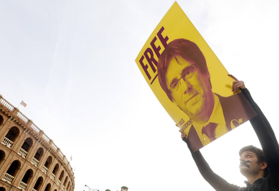 Un joven con la boca precintada lleva una pancarta del expresidente de la Generalitat Carles Puigdemont