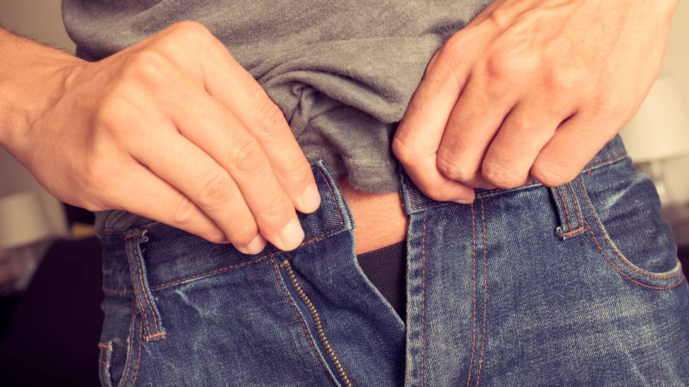 Una persona intenta abrocharse un botón del pantalón