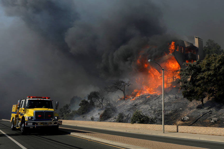 FILE PHOTO: A fire crew passes a burning home during a wind-driven wildfire in Ventura, California