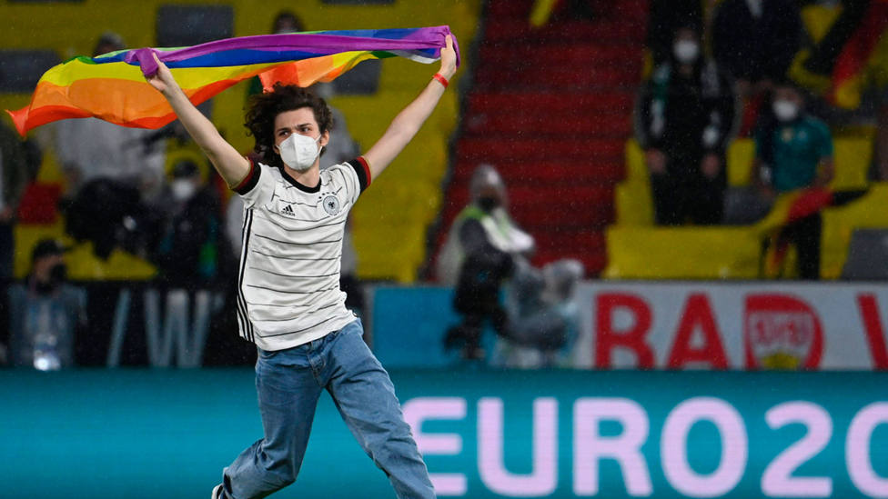 Un aficionado con la bandera LGTBI interrumpe un partido de fútbol portando una bandera del colectivo