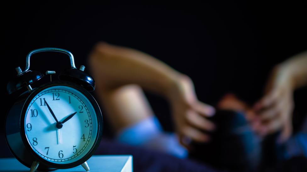 Una persona no puede dormir mientras el reloj marca altas horas de la noche