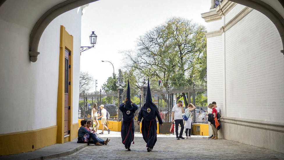 Dos nazarenos de la Hermandad de El Baratillo caminan por los exteriores de la Real Maestranza de Sevilla