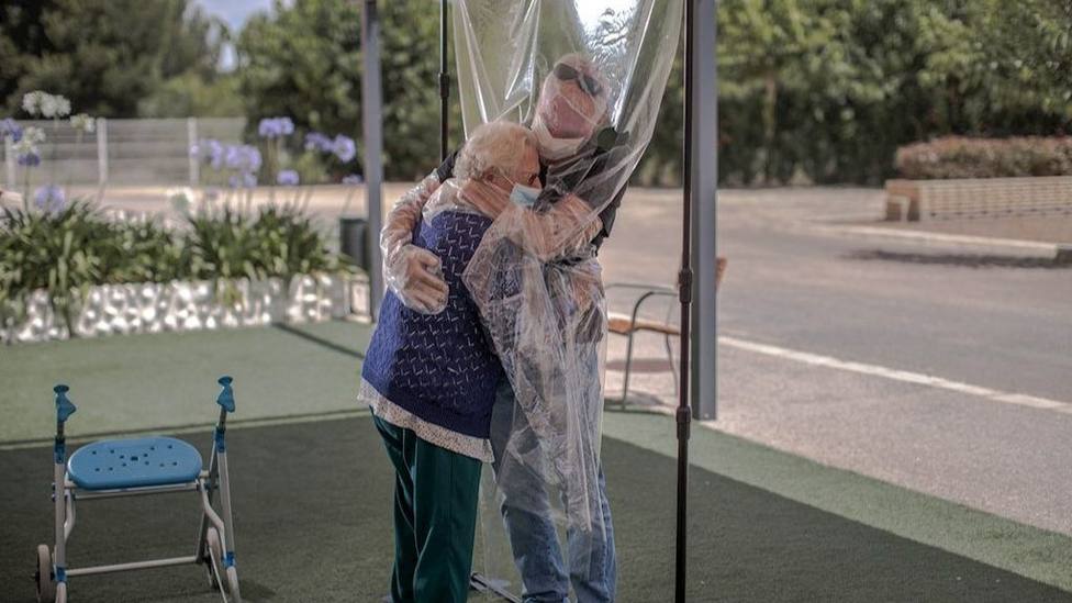 Una interna en una residencia de mayores abraza a su familiar a través de un plástico