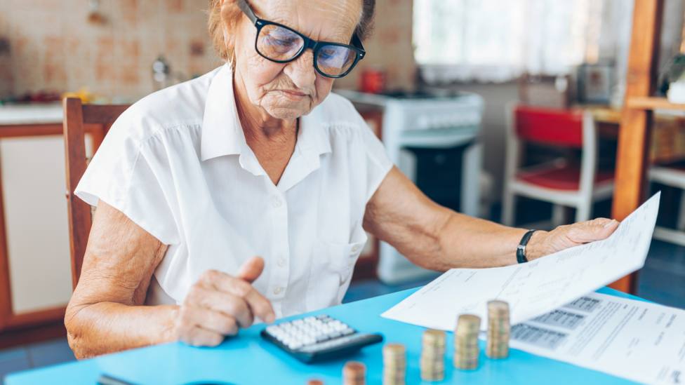 Una mujer comprueba sus recibos con varias monedas sobre una mesa