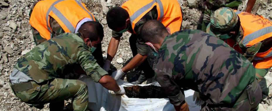 Miembros del ejército sirio removiendo un cuerpo de una tumba común (EFE)
