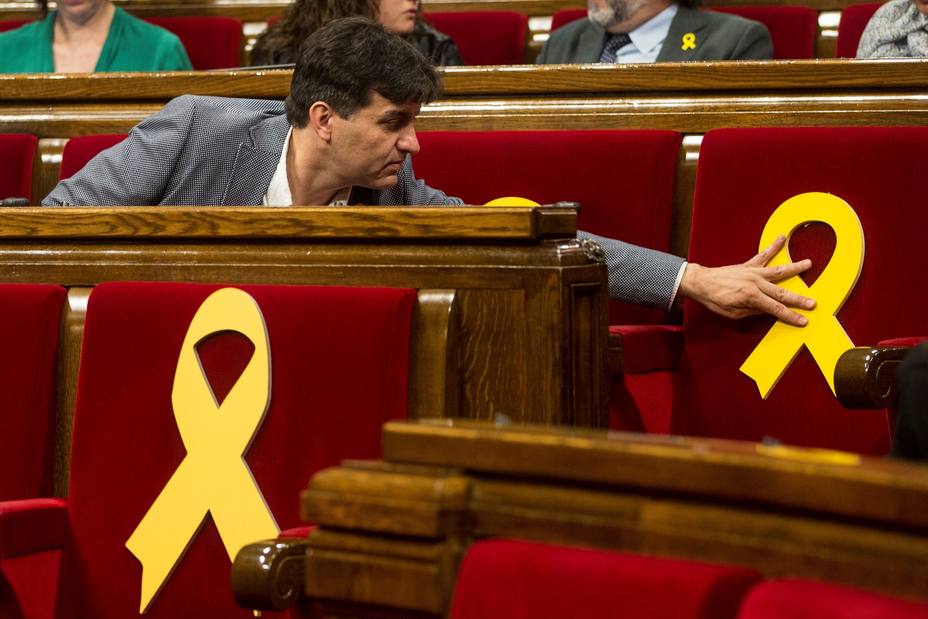 Sergi Sabrià (ERC) coloca un lazo amarillo en uno de los escaños vacios del Parlament. EFE