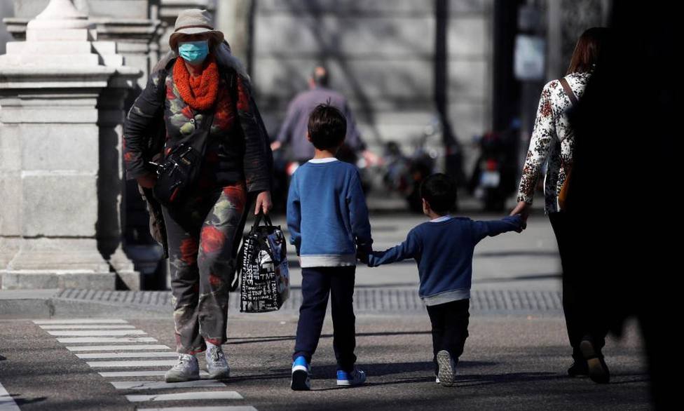 Un par de niños cruzan de la mano de su madre una calle en Madrid