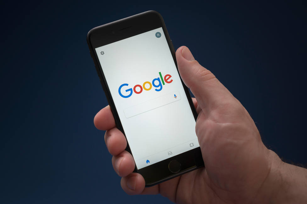 A man looks at his iPhone which displays the Google logo (Editorial use only).