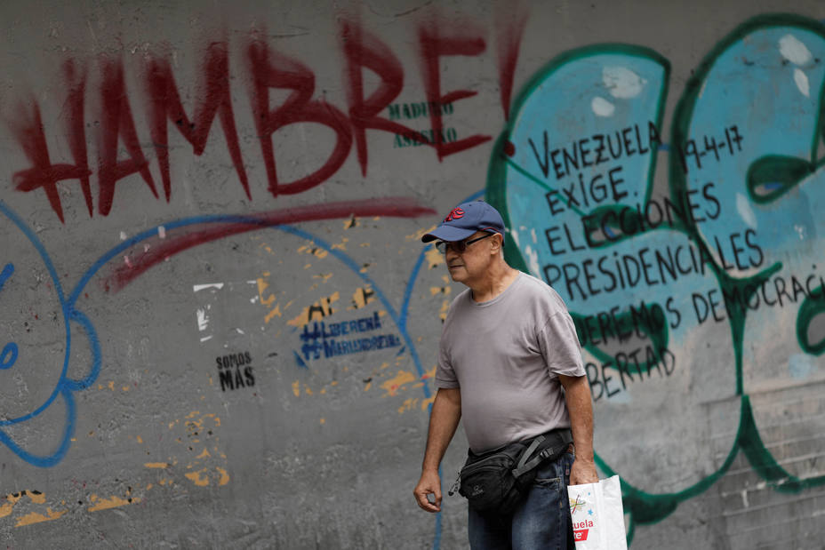 A man walks past of a wall with graffiti that reads hungry, in Caracas