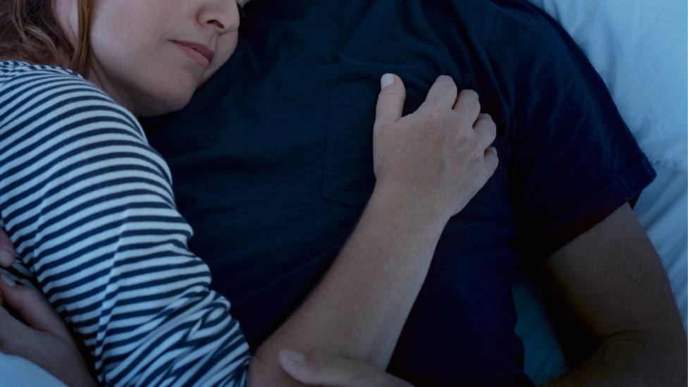 Una pareja se abraza mientras duerme en una cama